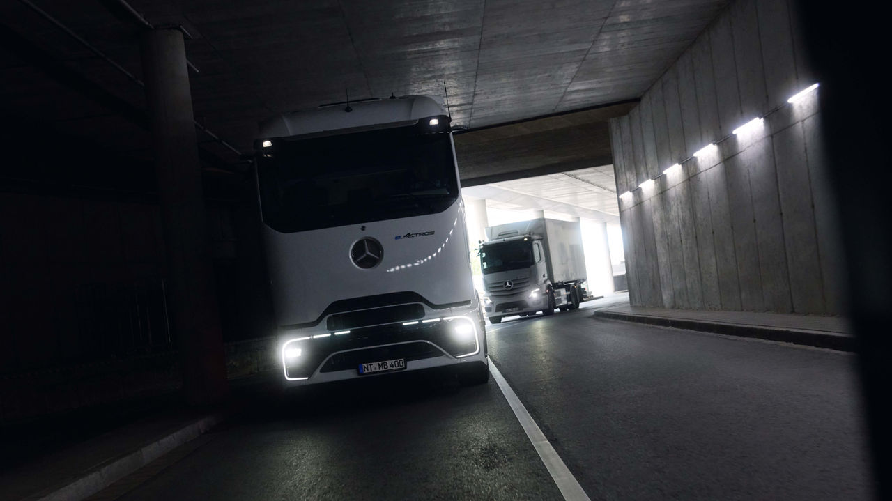 Zwei eActros 400, einer mit der ProCabin und einer mit bewährter Kabine, fahren durch einen dunklen Tunnel mit leuchtenden Scheinwerfern. Am Ende des Tunnels ist helles Tageslicht zu sehen, was einen Kontrast zur dunklen Umgebung bildet.